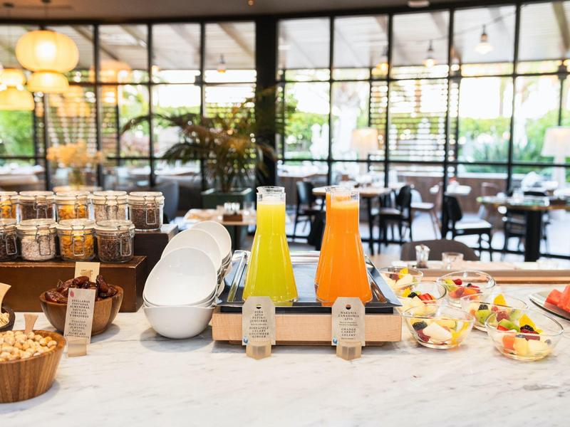 Ontbijtbalie met sapdispensers, granen en yoghurtbekers in een lichte eetruimte.