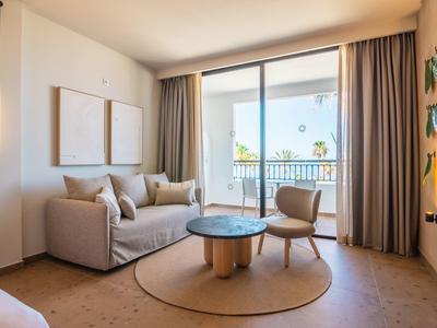 Przytulny salon z sofą, fotelem i dużym oknem z widokiem na balkon i zieleń.