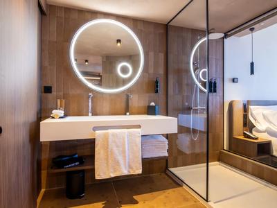 Nowoczesna łazienka z okrągłym podświetlanym lustrem i szklaną kabiną prysznicową w ciepłych drewnianych tonach