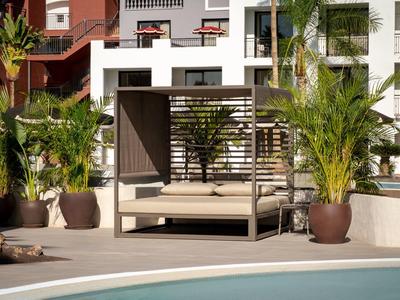 Nowoczesne łóżko na zewnątrz z osłoną przeciwsłoneczną i roślinami przy basenie hotelowym.