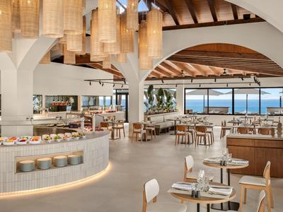 Jasna, nowoczesna restauracja z okrągłymi lampami, drewnianym sufitem i widokiem na morze.