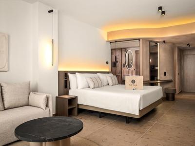 Nowoczesny pokój hotelowy z podwójnym łóżkiem, sofą i stylowym oświetleniem.