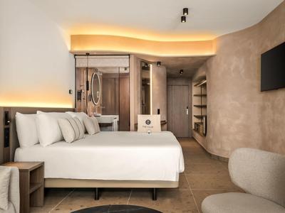 Nowoczesny pokój hotelowy z dużym łóżkiem, miękkimi poduszkami i pośrednim oświetleniem.