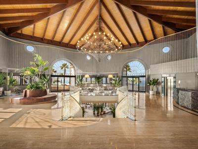 Großer Hotellobbybereich mit hölzernem Dach, Kronleuchter und Sitzgruppen in warmem Licht.