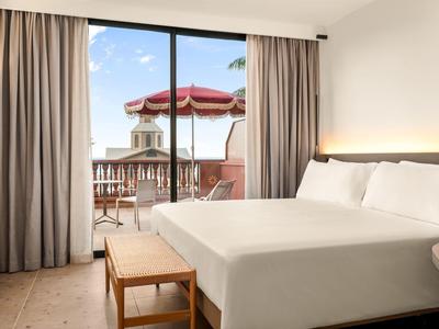 Sypialnia z dużym łóżkiem i balkonem z widokiem na taras z parasolem.