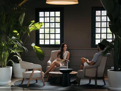 Due persone sedute in un elegante lounge d'hotel con grandi piante e finestre.