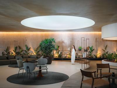 Lounge moderna con aree salotto circolari, piante e una grande finestra zenitale in un hotel