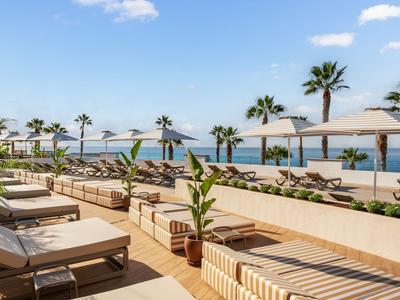Terrazza moderna dell'hotel con lettini, ombrelloni e vista sul mare sotto un cielo azzurro.