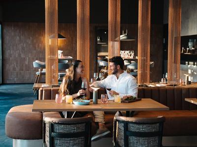 Due persone che chiacchierano bevendo a un tavolo di legno in un elegante bar dell'hotel.