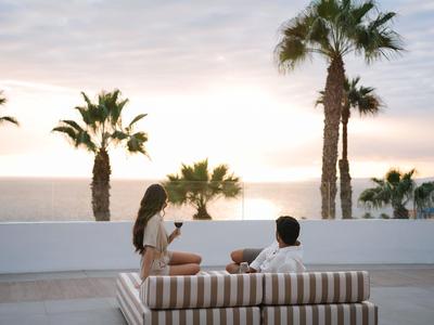 Coppia si rilassa su una terrazza con palme e il mare sullo sfondo al tramonto.