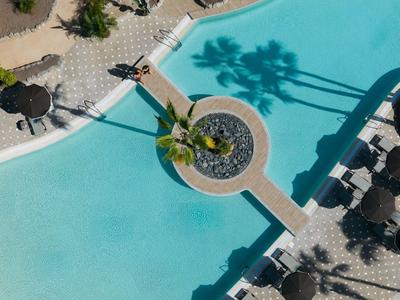 Vista aerea di una piscina con un ponte e ombrelloni nel giardino dell'hotel