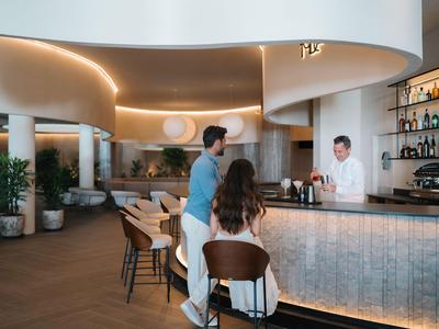 Interno moderno di un bar d'hotel con ospiti e barista in un ambiente elegante.