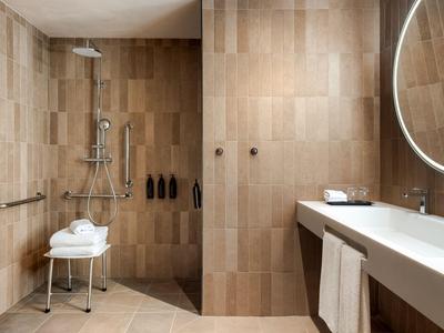 Bagno moderno con pareti piastrellate beige, doccia a pavimento e grande specchio illuminato.