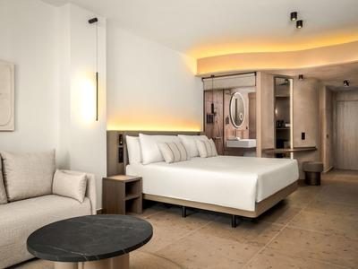 Camera d'albergo moderna con letto grande, divano, tavolo rotondo e illuminazione indiretta.