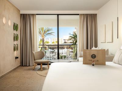 Camera d'hotel luminosa con letto grande e vista sul balcone con palme.