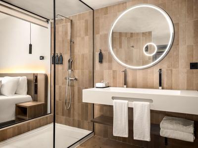 Bagno moderno con specchio rotondo illuminato, lavandino bianco e pareti in legno.