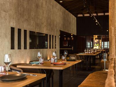 Ristorante moderno con tavoli in legno, sedie in pelle marrone e illuminazione calda.