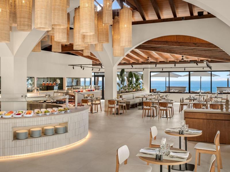 Jasna, nowoczesna restauracja z okrągłymi lampami, drewnianym sufitem i widokiem na morze.