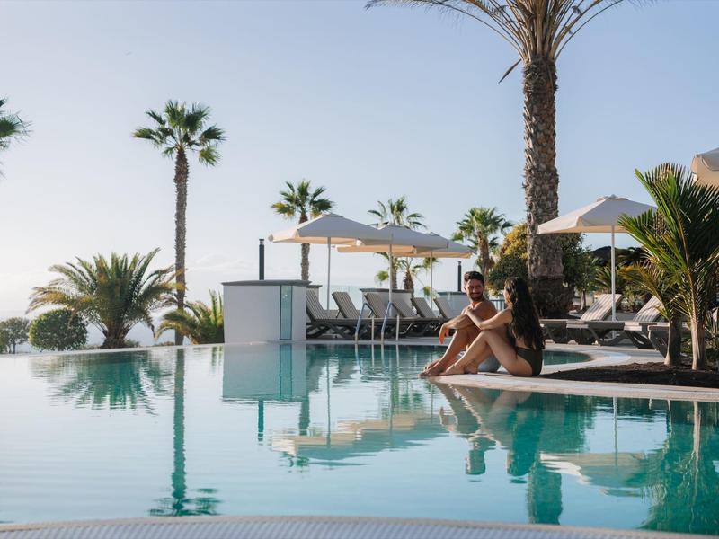 Kobieta relaksująca się przy hotelowym basenie z palmami i leżakami w tle.