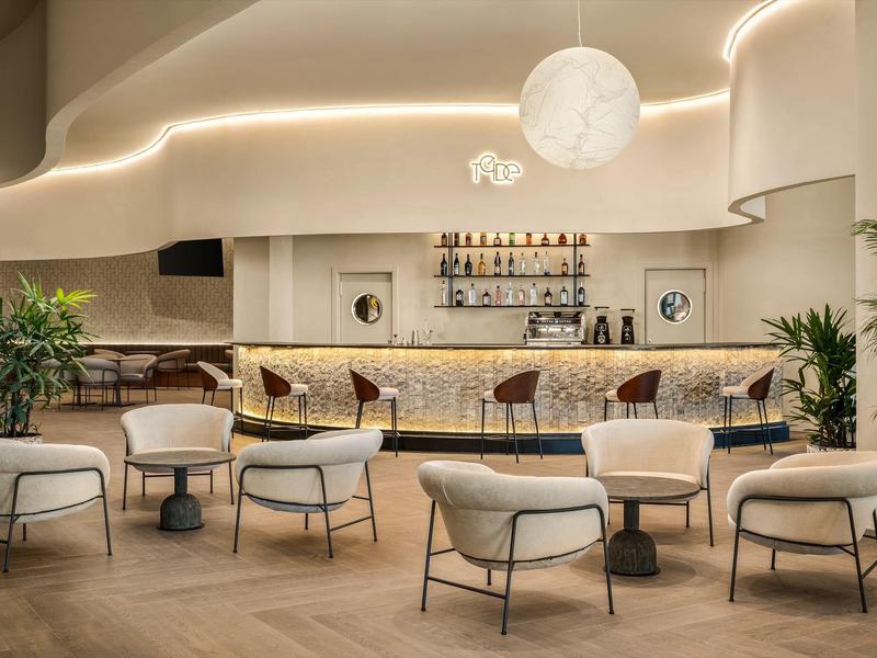 Nowoczesny bar hotelowy z wygodnymi fotelami, stołami i podświetlanym barem.