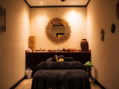 Przytulny, ciepło oświetlony pokój do masażu z dekoracyjnym lustrem i relaksującymi dodatkami.