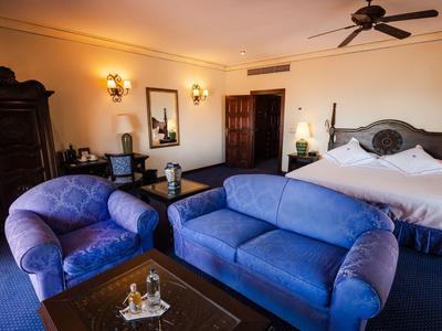 Cozy hotel room with blue sofa, armchair, large bed, and classic wooden furniture.