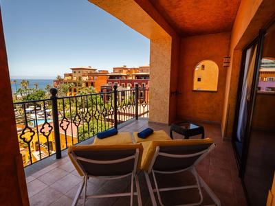 Balcony with two chairs and table, view of hotel pool and sea in the background.
