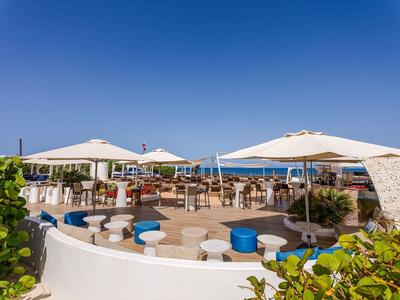 Nowoczesny taras hotelowy na zewnątrz z okrągłymi stołami, krzesłami i białymi parasolami pod czystym niebem.