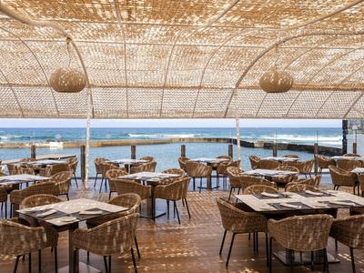 Otwarta restauracja na plaży z wiklinowymi krzesłami pod zacienionym dachem z widokiem na morze.