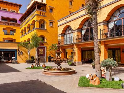 Kolorowe dziedzińce hotelu z fontanną i dekoracyjnymi roślinami pod jasnym niebem.