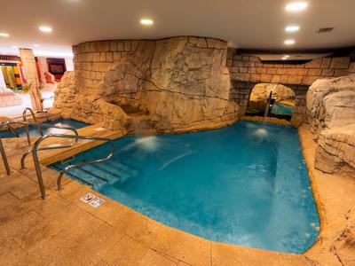 Basen kryty z kamiennymi ścianami i niebieską wodą, schodami do wejścia i jasnym oświetleniem sufitowym.