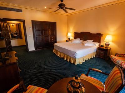 Przytulny pokój hotelowy z dużym łóżkiem, wykładziną i częścią wypoczynkową z stołem i krzesłami.