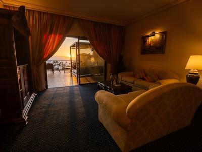 Przytulny pokój hotelowy z sofą, szafką na telewizor i tarasem z widokiem na morze o zachodzie słońca.