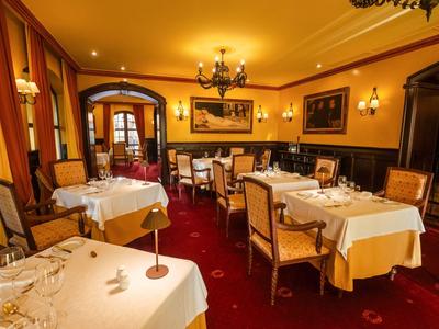 Elegancka sala restauracyjna hotelu z nakrytymi stolikami, ciepłym oświetleniem i czerwonym dywanem.