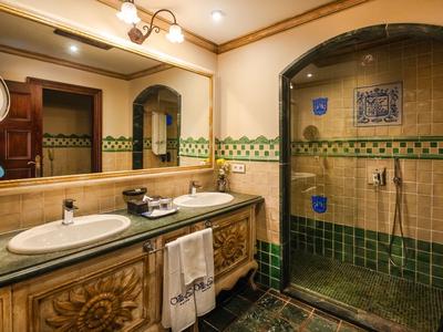 Luxurious bathroom with wooden vanity, mirrors, and walk-in shower with green and brown tiles.
