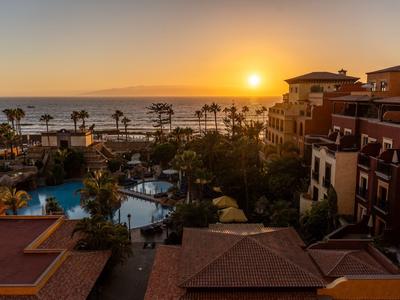 Sunset over a hotel with pool, palm trees, and sea view.