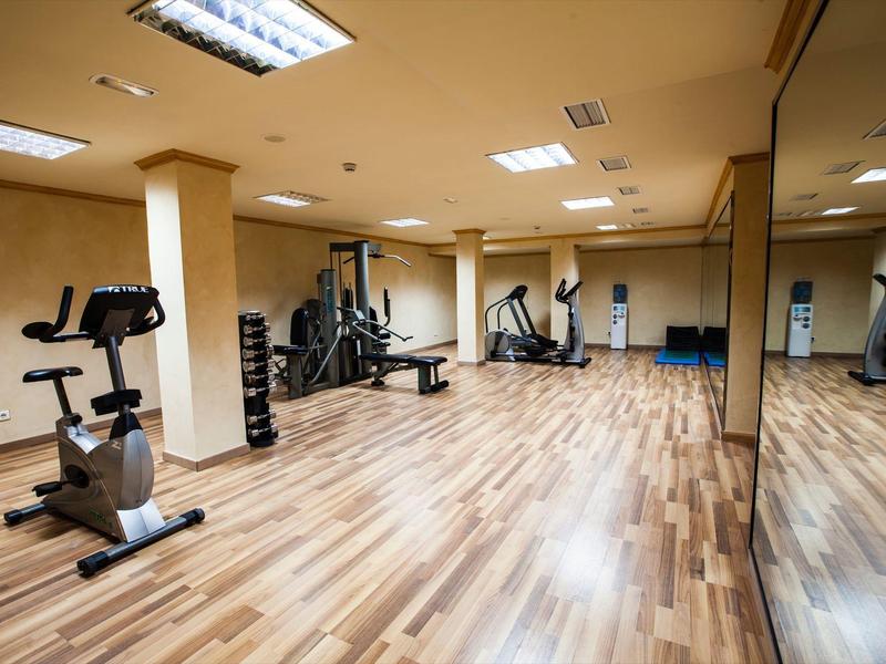 Nowoczesna siłownia z drewnianą podłogą i różnym sprzętem do ćwiczeń.
