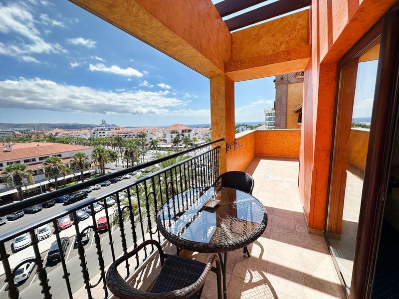 Balkon z szklanym stołem i krzesłem z widokiem na miasto i morze w słoneczny dzień.