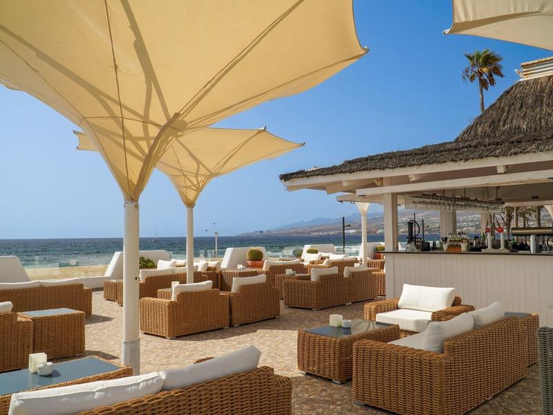 Hotel nad morzem z wygodnymi meblami z wikliny, parasolami i widokiem na morze pod niebieskim niebem.