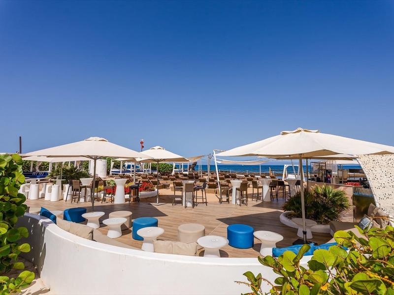 Nowoczesny taras hotelowy na zewnątrz z okrągłymi stołami, krzesłami i białymi parasolami pod czystym niebem.