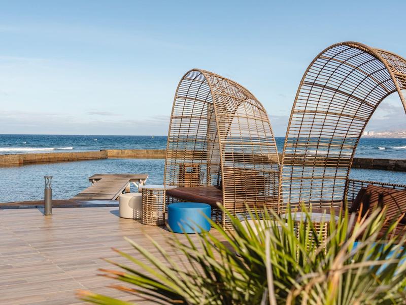 Drewniany taras z nowoczesnymi wiklinowymi siedzeniami i widokiem na morze pod bezchmurnym niebem.