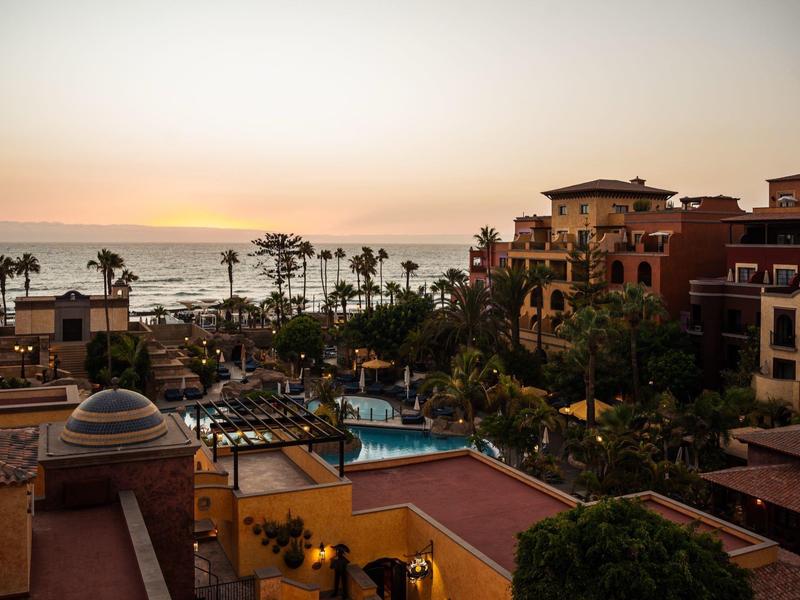 Widok na basen hotelowy i palmy o zachodzie słońca nad morzem.