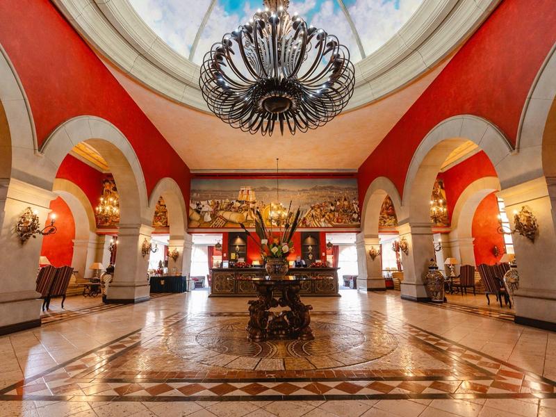 Wielka lobby hotelowa z wysokimi łukami, czerwonymi ścianami i dużym żyrandolem.