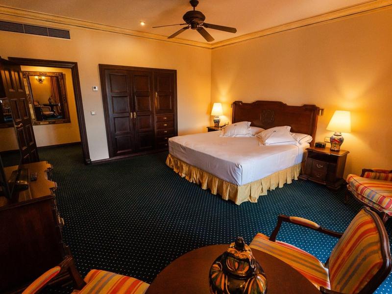 Przytulny pokój hotelowy z dużym łóżkiem, wykładziną i częścią wypoczynkową z stołem i krzesłami.