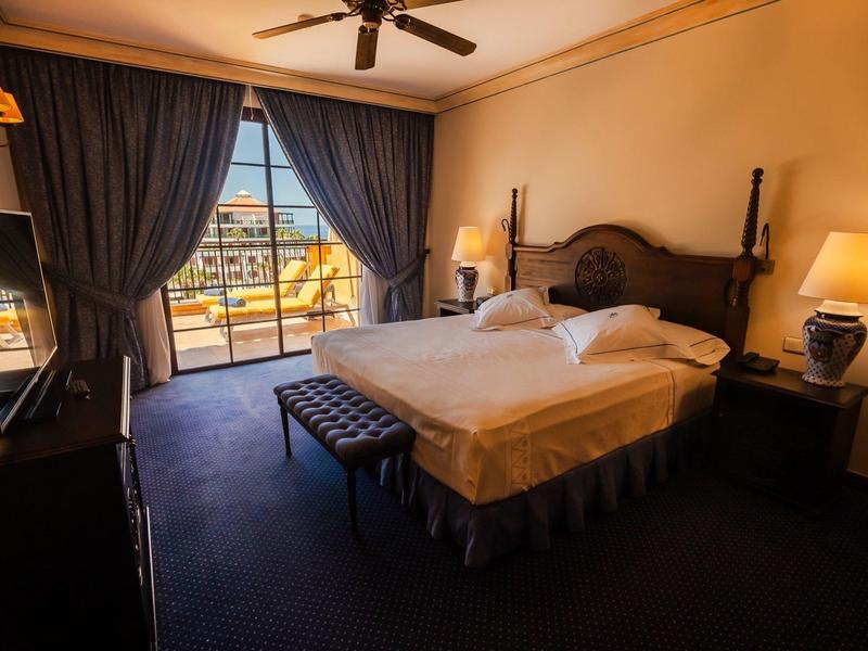 Przytulny pokój hotelowy z podwójnym łóżkiem, ciemnoniebieskimi zasłonami i balkonem z widokiem.