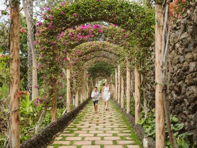 Deux personnes marchent le long d'un chemin de jardin bordé d'arcs fleuris et de pavés.