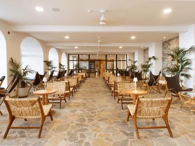 Ristorante moderno e luminoso con pavimento in pietra, sedie in legno e piante ai lati