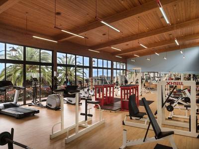 Grande salle de sport avec plafond en bois, nombreuses machines d'entraînement et grandes fenêtres donnant sur l'extérieur.