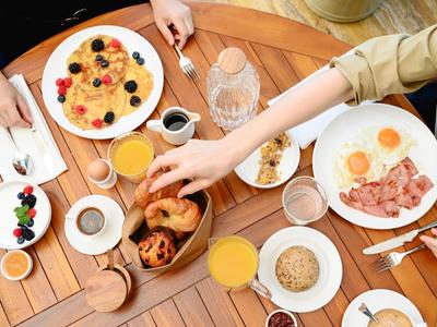 Tavolo per la colazione con pancake, uova, croissant, succo d'arancia e caffè condivisi tra persone.