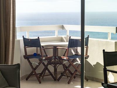 Balcone con piccolo tavolo di legno e sedie con vista sul mare sotto un cielo nuvoloso.